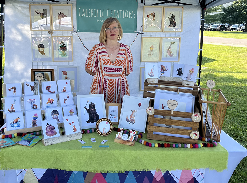 Callie Hastings standing behind her booth at the waterbury , Vermont arts festival